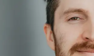 Zbliżenie na oko i fragment twarzy mężczyzny z brązowymi brwiami i zarostem.