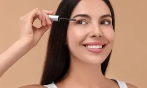 Uśmiechnięta kobieta nakłada odżywkę na rzęsy.
