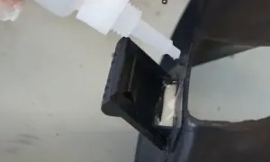Kropla kleju cyjanoakrylowego kapie z białej butelki na czarny plastik.
