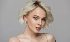 Portret młodej kobiety z krótkimi blond włosami i niebieskimi oczami, z delikatnym makijażem.