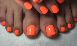 Paznokcie u nóg neonowe, w intensywnym pomarańczowym kolorze, przyciągają wzrok. Idealny manicure na lato.