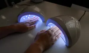 Dwie dłonie z różowym lakierem żelowym utwardzają się w lampach UV.