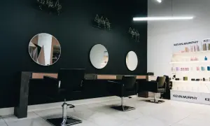 Nowoczesne wnętrze salonu fryzjerskiego z czarnymi fotelami, lustrami i półkami z kosmetykami.
