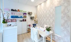 Jasny, schludny gabinet kosmetyczny z białymi meblami, półkami z produktami i stołem do manicure.