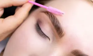 Stylist układa brwi po laminacji różową szczoteczką. Zastanawiasz się, jaki olejek po laminacji brwi będzie najlepszy?