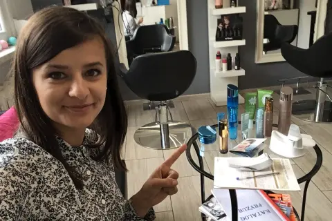 Kobieta w salonie kosmetycznym wskazuje na stolik z kosmetykami i katalogiem.