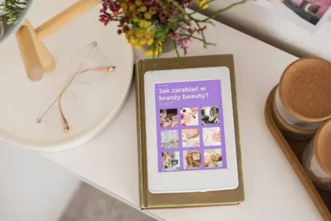 E-book "Jak zarabiać w branży beauty?" na tablecie. Obok okulary i bukiet kwiatów. Idealne inspiracje dla każdej stylistki.
