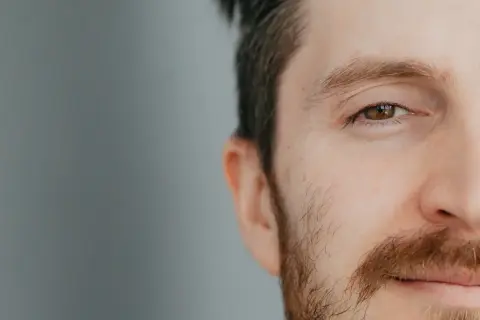 Zbliżenie na oko i fragment twarzy mężczyzny z brązowymi brwiami i zarostem.