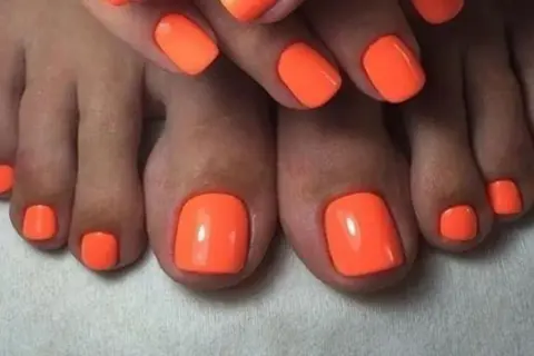 Paznokcie u nóg neonowe, w intensywnym pomarańczowym kolorze, przyciągają wzrok. Idealny manicure na lato.