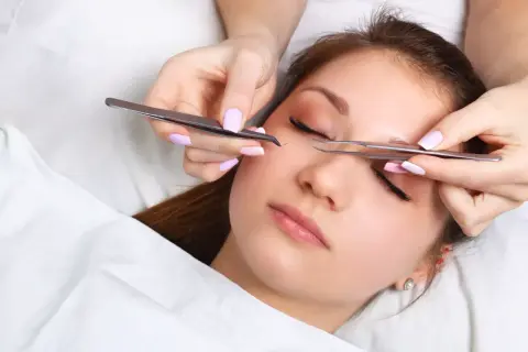 Stylistka precyzyjnie dokłada rzęsy klientce za pomocą pęset.