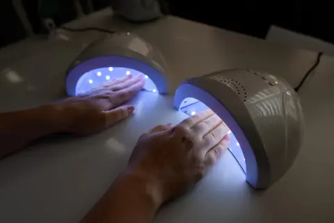 Dwie dłonie z różowym lakierem żelowym utwardzają się w lampach UV.