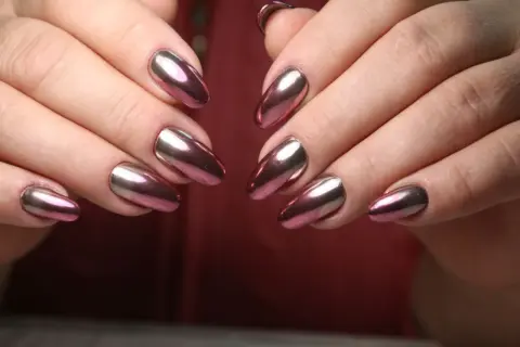 Dłonie z paznokciami w stylu lustrzane baby boomer. Kolorowy, metaliczny połysk odbija światło, tworząc efektowny manicure.