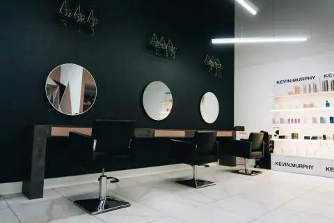 Nowoczesne wnętrze salonu fryzjerskiego z czarnymi fotelami, lustrami i półkami z kosmetykami.