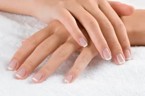 Dłonie z klasycznym french manicure. Delikatny róż i biel sprawiają, że palce wyglądają na dłuższe i smuklejsze. Jaki kolor paznokci wyszczupla palce? Ten subtelny french manicure!