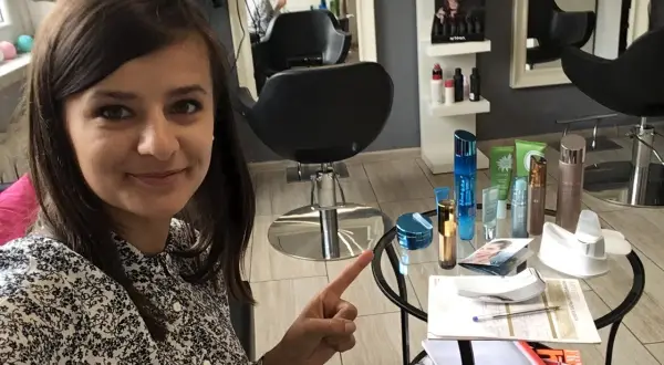 Kobieta w salonie kosmetycznym wskazuje na stolik z kosmetykami i katalogiem.
