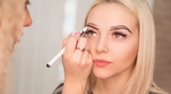 Stylistka brwi precyzyjnie rysuje kontur na łuku brwiowym klientki.