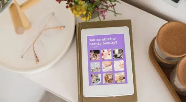E-book "Jak zarabiać w branży beauty?" na tablecie. Obok okulary i bukiet kwiatów. Idealne inspiracje dla każdej stylistki.