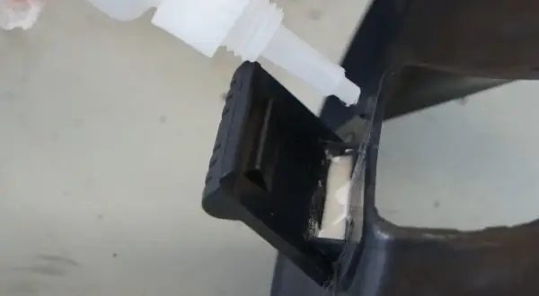 Kropla kleju cyjanoakrylowego kapie z białej butelki na czarny plastik.