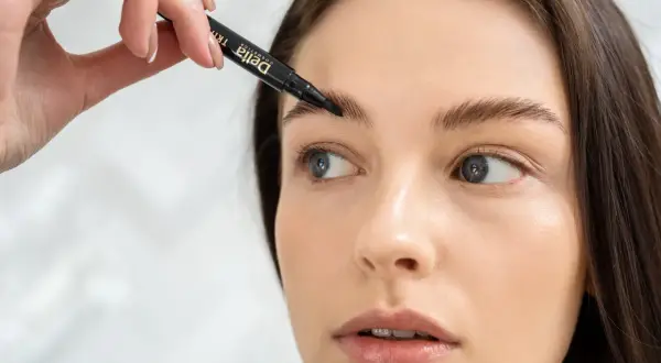 Kobieta aplikuje produkt do brwi za pomocą czarnego pisaka.