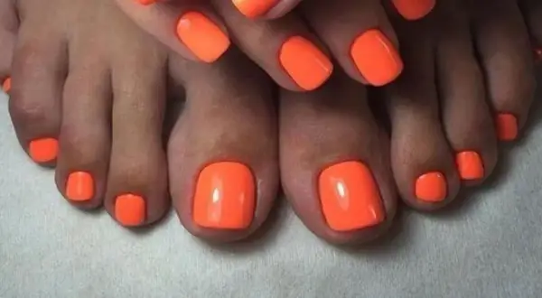 Paznokcie u nóg neonowe, w intensywnym pomarańczowym kolorze, przyciągają wzrok. Idealny manicure na lato.