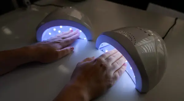 Dwie dłonie z różowym lakierem żelowym utwardzają się w lampach UV.