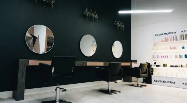 Nowoczesne wnętrze salonu fryzjerskiego z czarnymi fotelami, lustrami i półkami z kosmetykami.