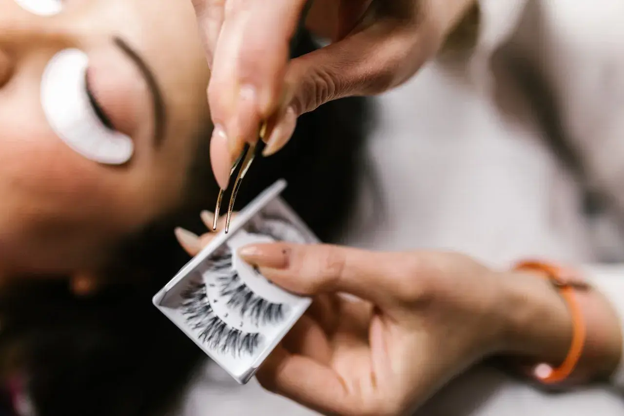 Zbliżenie na dłoń trzymającą pęsetą sztuczne rzęsy z opakowania.
