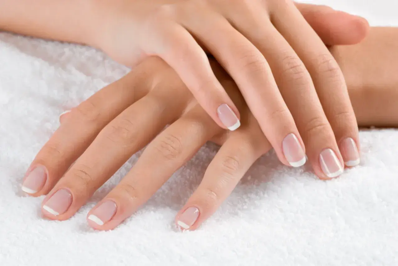 Dłonie z klasycznym french manicure. Delikatny róż i biel sprawiają, że palce wyglądają na dłuższe i smuklejsze. Jaki kolor paznokci wyszczupla palce? Ten subtelny french manicure!