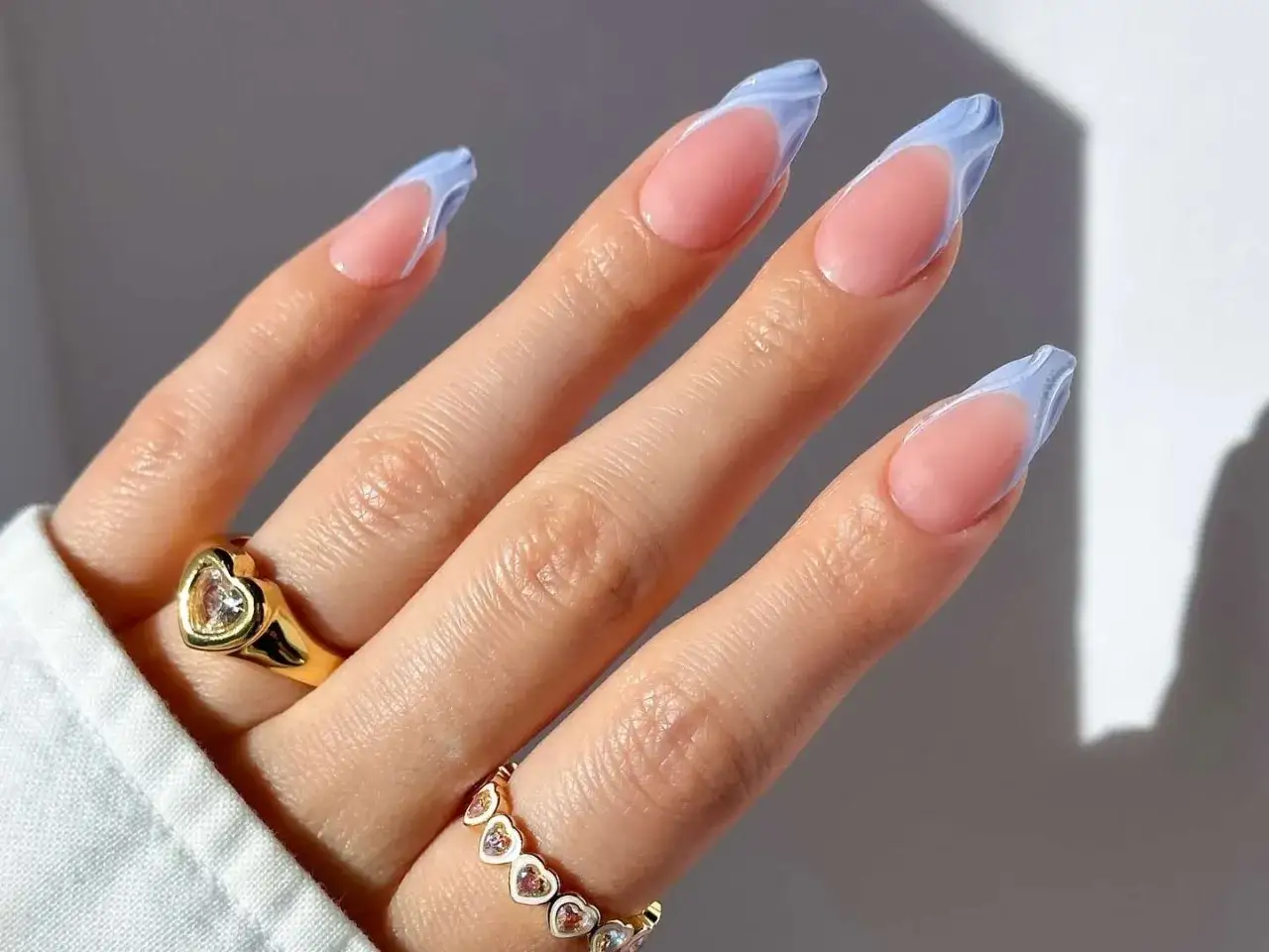 Dłoń z paznokciami w stylu francuskiego manicure z błękitnymi, falowanymi końcówkami. Różne rodzaje tipsów pozwalają na kreatywne zdobienia.
