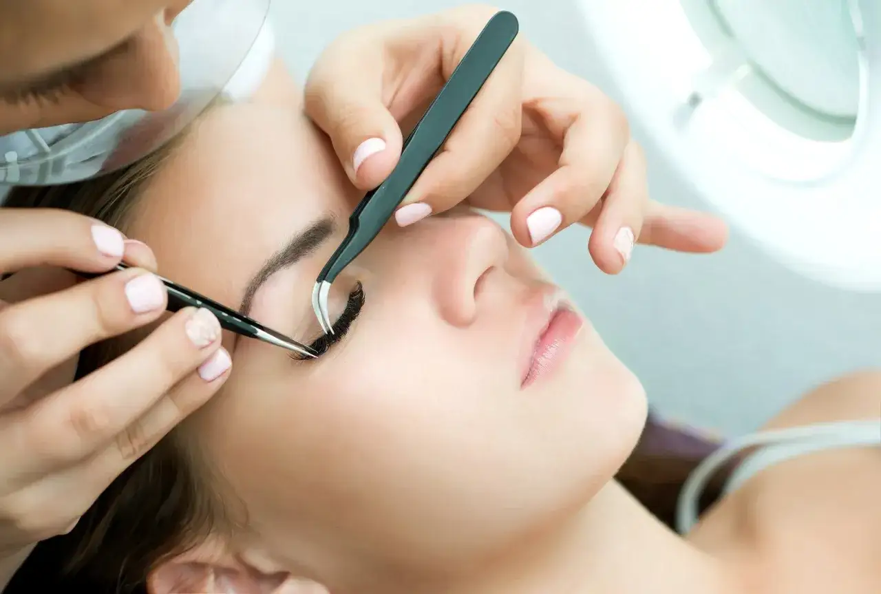 Dłoń stylistki precyzyjnie dokłada rzęsy. Marzysz o karierze w branży beauty? Sprawdź, jak uzyskać kurs przedłużania rzęs dofinansowanie.