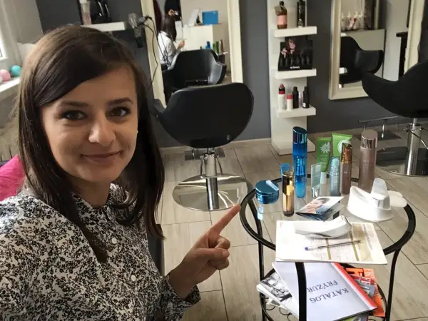 Kobieta w salonie kosmetycznym wskazuje na stolik z kosmetykami i katalogiem.