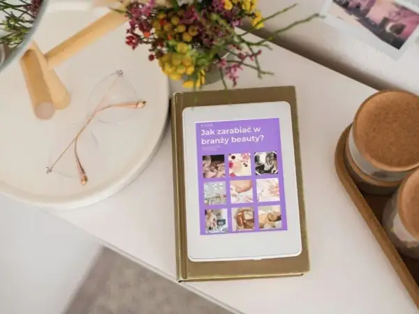 E-book "Jak zarabiać w branży beauty?" na tablecie. Obok okulary i bukiet kwiatów. Idealne inspiracje dla każdej stylistki.