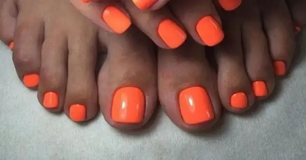 Paznokcie u nóg neonowe, w intensywnym pomarańczowym kolorze, przyciągają wzrok. Idealny manicure na lato.