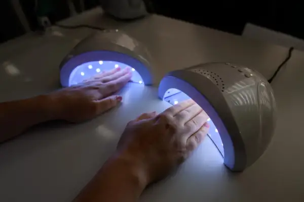 Dwie dłonie z różowym lakierem żelowym utwardzają się w lampach UV.