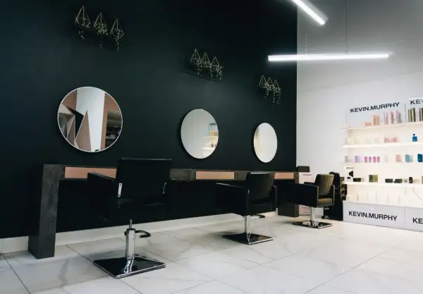 Nowoczesne wnętrze salonu fryzjerskiego z czarnymi fotelami, lustrami i półkami z kosmetykami.