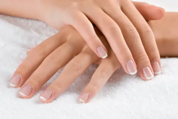 Dłonie z klasycznym french manicure. Delikatny róż i biel sprawiają, że palce wyglądają na dłuższe i smuklejsze. Jaki kolor paznokci wyszczupla palce? Ten subtelny french manicure!